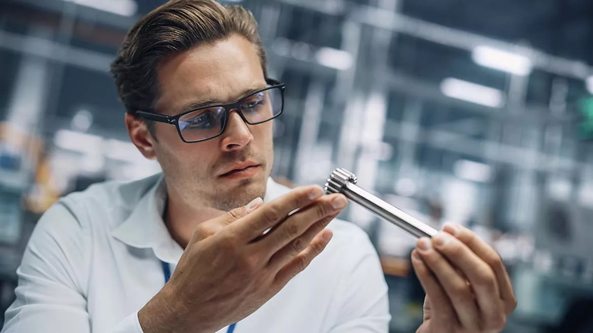Close-up of a young engineer in glasses, working on manufacturing metal parts at a car assembly plant.