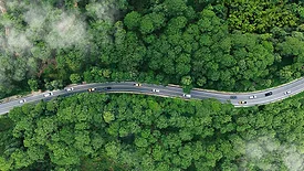 Aerial view of cars on a windy road driving through a lush and misty forest.
