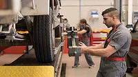 Two Mechanics calibrating wheels with computer and technology equipment.
