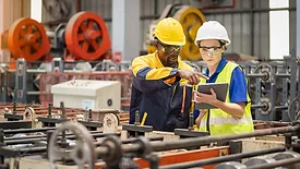 Industrial workers inspecting machinery and discussing workflow on a production line, the factory background is blurred.