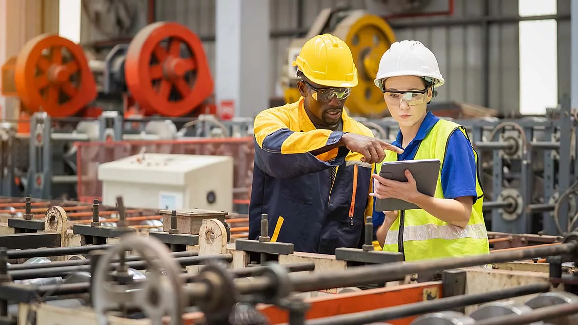 Industrial workers inspecting machinery and discussing workflow on a production line, the factory background is blurred.