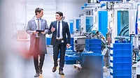Engineer in a grey coat walking with company CEO through a factory.