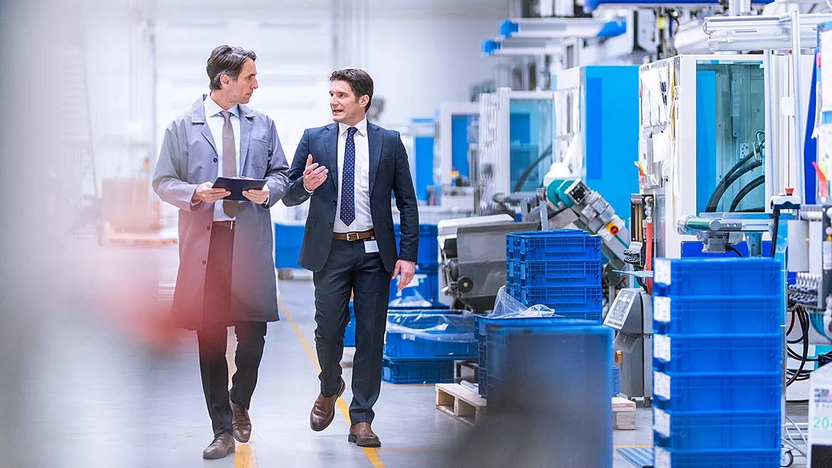 Engineer in a grey coat walking with company CEO through a factory.