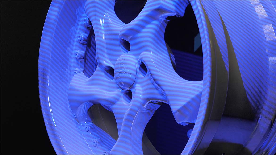 Highly polished car wheel rim matted with scanning spray, dimly lit with a purplish glow.