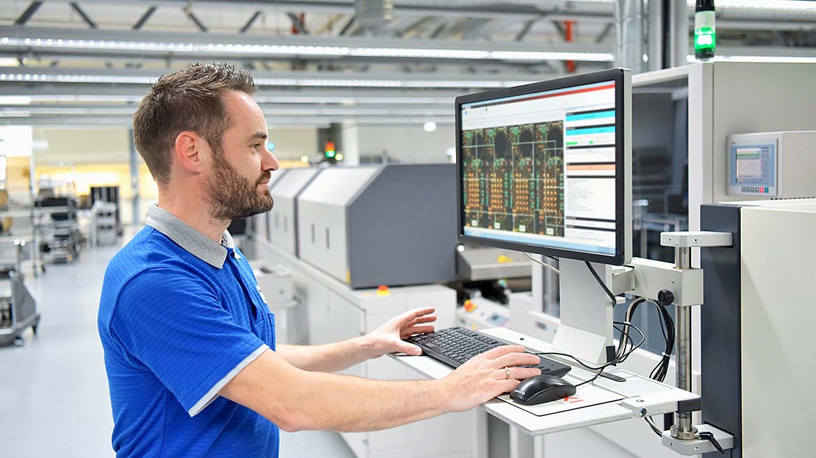 Engineer working on a computer while standing, inside a modern factory.