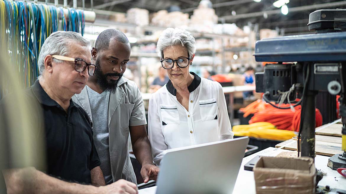 Coworkers using laptop and working together in factory, with a blurred background.