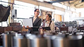 Female professionals discuss manufacturing infrastructure investment project in modern factory.