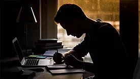 a silhouette of a person studying at a desk
