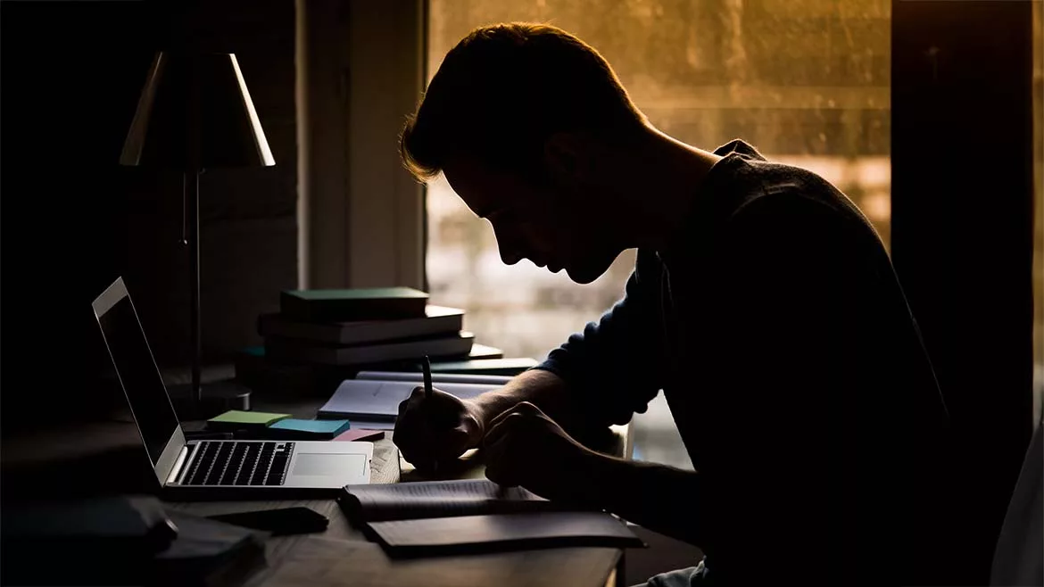 a silhouette of a person studying at a desk