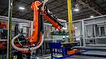 The image shows a KUKA industrial robot operating within an automated manufacturing facility