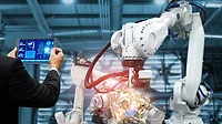 The image illustrates industrial robotic automation controlled by a manager or engineer using a tablet.