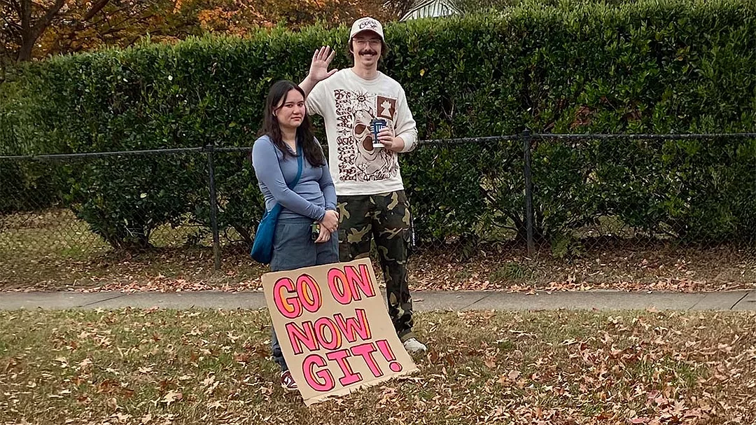 two people standing outside with a sign that says "GO ON NOW GIT!"