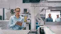 a woman using a tablet in a manufacturing or industrial setting, suggesting the use of technology for operational management