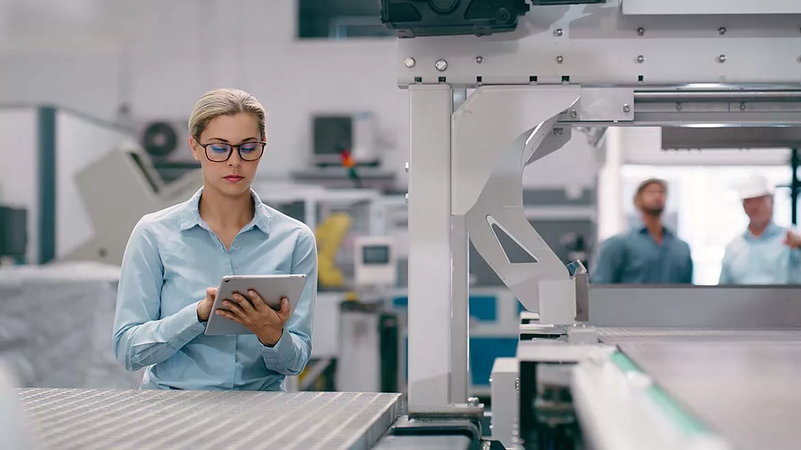 a woman using a tablet in a manufacturing or industrial setting, suggesting the use of technology for operational management