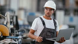 This image shows a man in a factory setting with a laptop