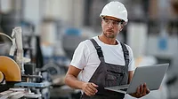 This image shows a man in a factory setting with a laptop