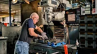 The image shows a machinist operating a CNC (Computer Numerical Control) milling machine