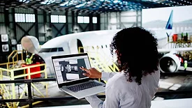 This image depicts a professional using technology for aviation maintenance, likely involving digital tools for managing or monitoring aircraft systems