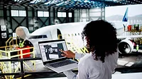 This image depicts a professional using technology for aviation maintenance, likely involving digital tools for managing or monitoring aircraft systems