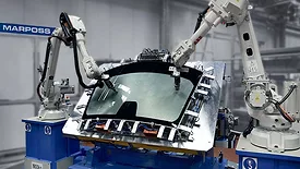 The image displays an industrial automation scene featuring robotic arms, specifically manufactured by ABB, performing tasks on a glass component. 