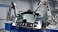 The image displays an industrial automation scene featuring robotic arms, specifically manufactured by ABB, performing tasks on a glass component. 