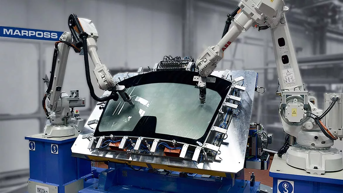 The image displays an industrial automation scene featuring robotic arms, specifically manufactured by ABB, performing tasks on a glass component.