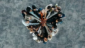 The image depicts a diverse business group standing in a heart formation, symbolizing unity, teamwork, and collaboration
