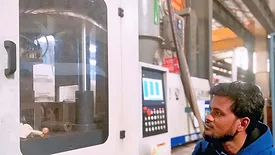 This image shows an industrial worker monitoring a plastic injection molding machine. 