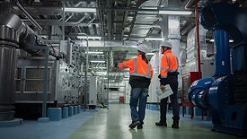This image shows two engineers in high-visibility safety vests and hard hats inspecting industrial machinery. 