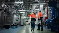 This image shows two engineers in high-visibility safety vests and hard hats inspecting industrial machinery. 