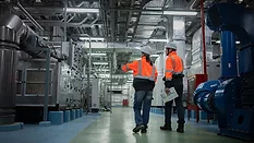 This image shows two engineers in high-visibility safety vests and hard hats inspecting industrial machinery. 