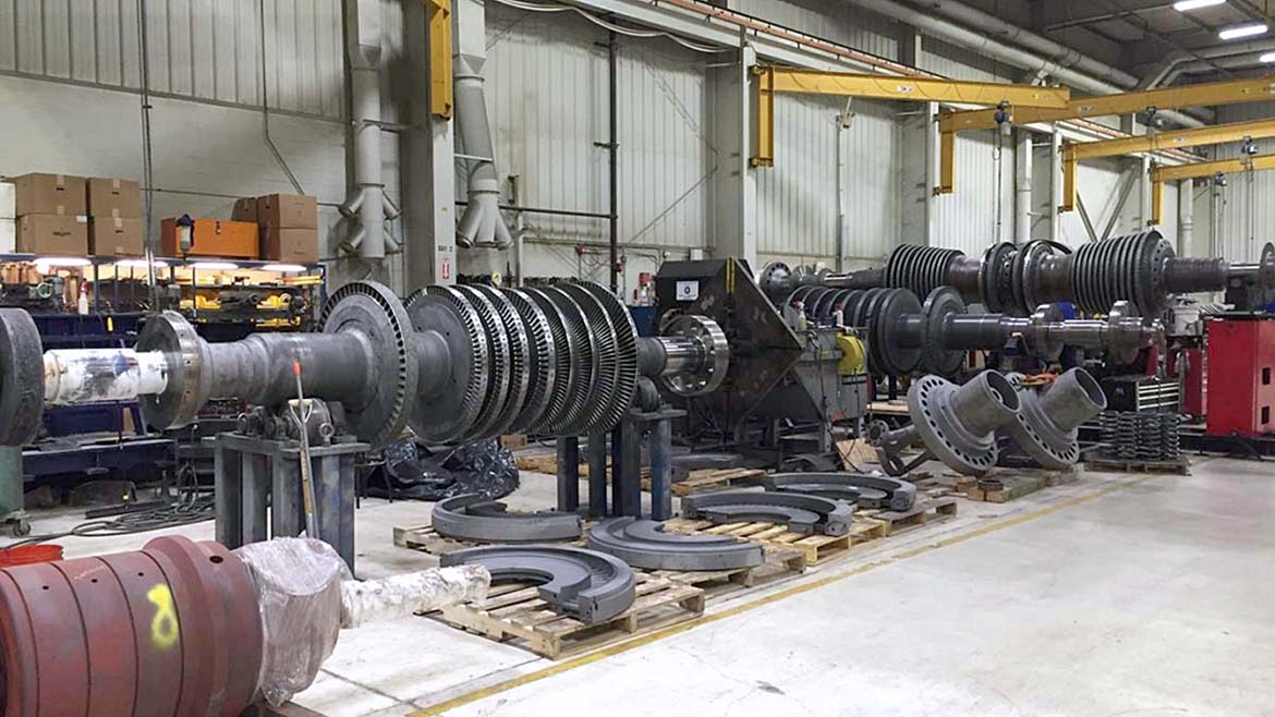 The image displays a gas turbine rotor undergoing maintenance or assembly in a service center. 