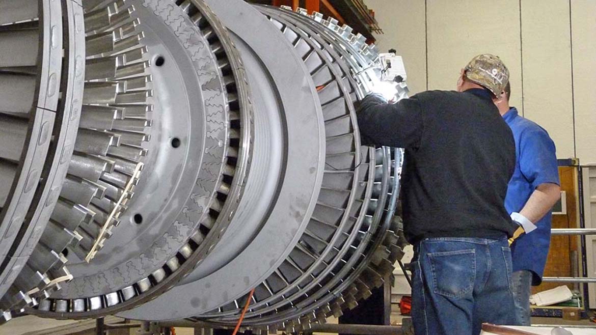 The image shows technicians working on a large gas turbine rotor assembly