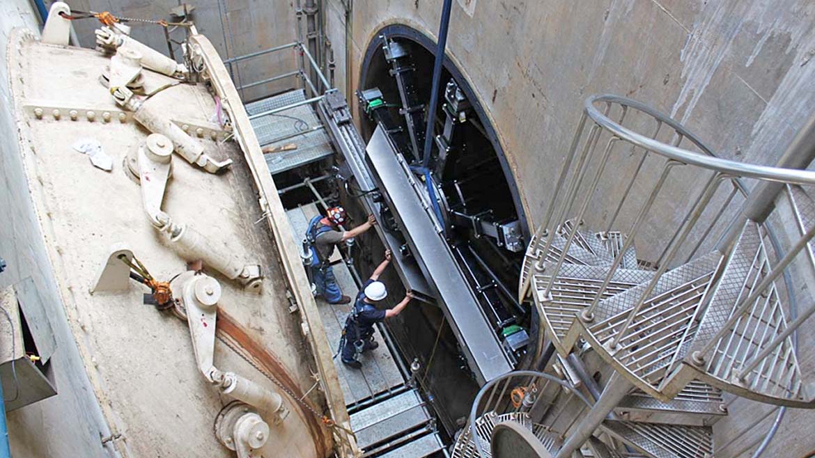 The image shows a tunnel boring machine (TBM) being assembled or operated in an access shaft.