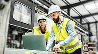 The image depicts two industrial workers in a manufacturing setting The image depicts two industrial workers in a manufacturing setting