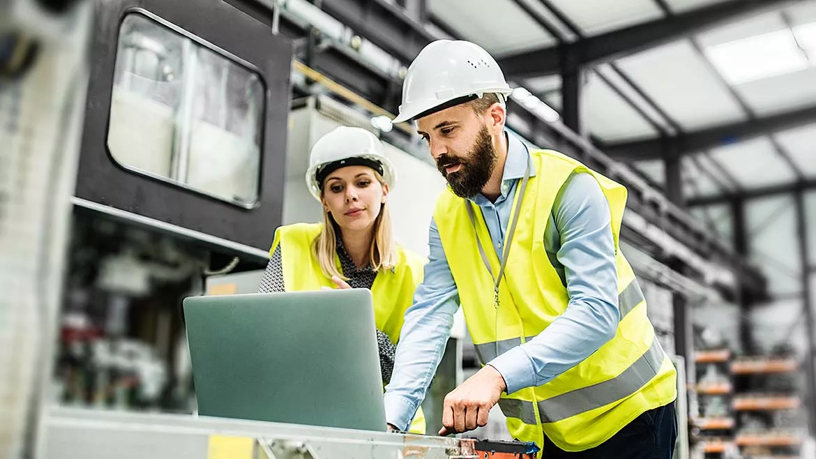The image depicts two industrial workers in a manufacturing setting