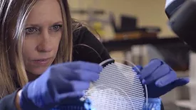 This image shows a manufacturing employee inspecting a MEMS glass wafer, which is a component used in medical equipment like ventilators. Bullen-p1FT-Bullen---Bullen-inspection-of-ultrasonically-machined-CVD-Silicon-Carbide.jpg