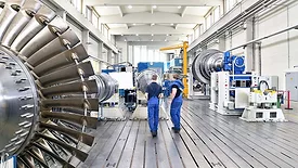 The image displays the assembly or manufacturing process of industrial gas turbines within a factory setting. 