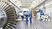 The image displays the assembly or manufacturing process of industrial gas turbines within a factory setting. 