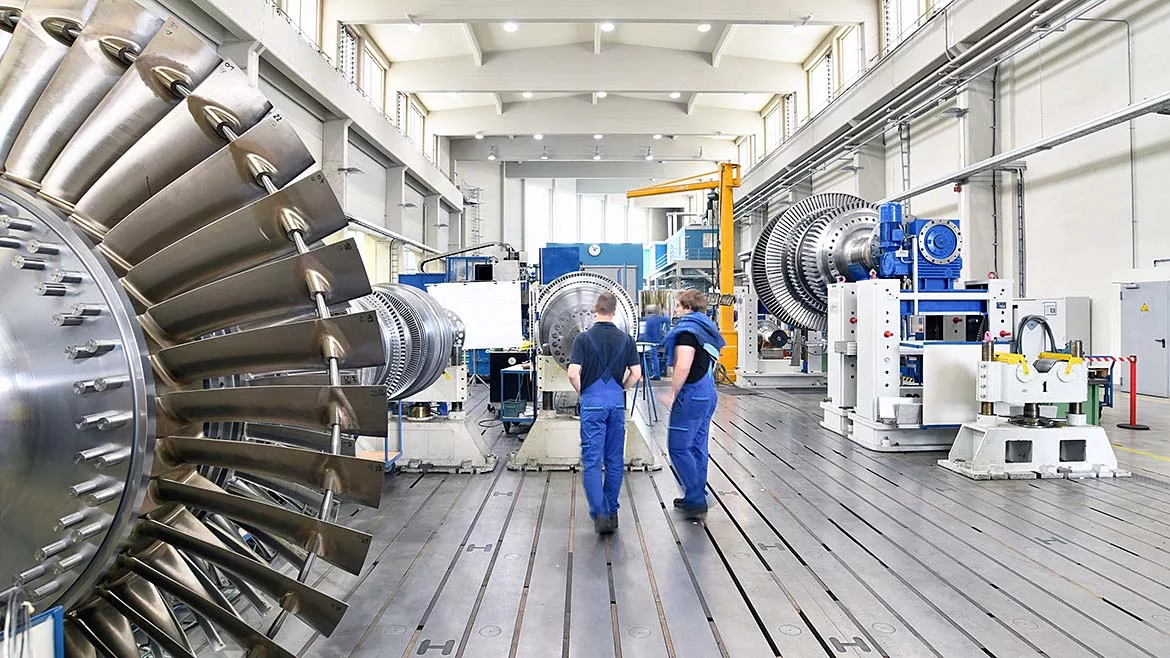 The image displays the assembly or manufacturing process of industrial gas turbines within a factory setting.