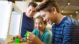 This image shows a consumer-grade 3D printer being used in an educational or makerspace setting. 