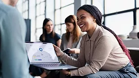 This image shows a business meeting where a person is presenting data from a laptop screen to colleagues.