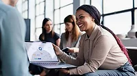 This image shows a business meeting where a person is presenting data from a laptop screen to colleagues.