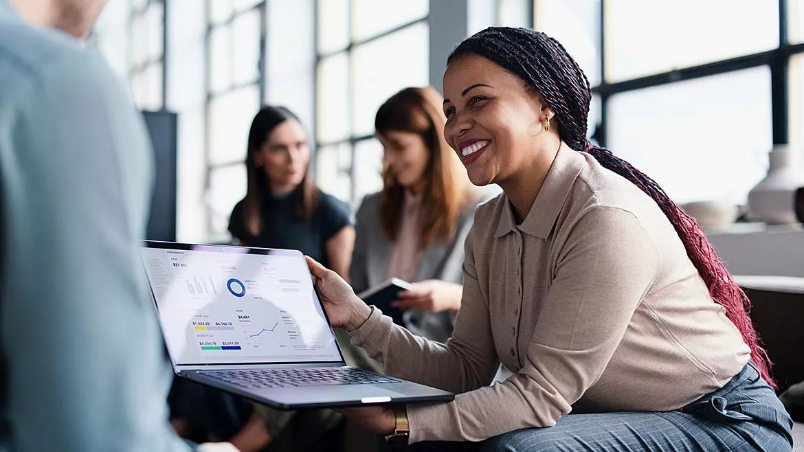 This image shows a business meeting where a person is presenting data from a laptop screen to colleagues.