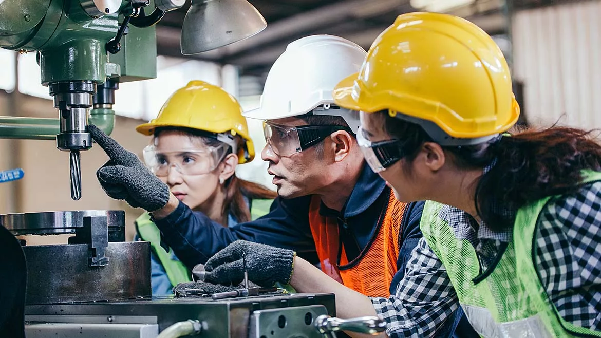 This image shows factory workers receiving on-the-job training to learn how to operate manufacturing machinery safely and effectively.