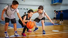 This image shows young children practicing basketball in an indoor gymnasium.