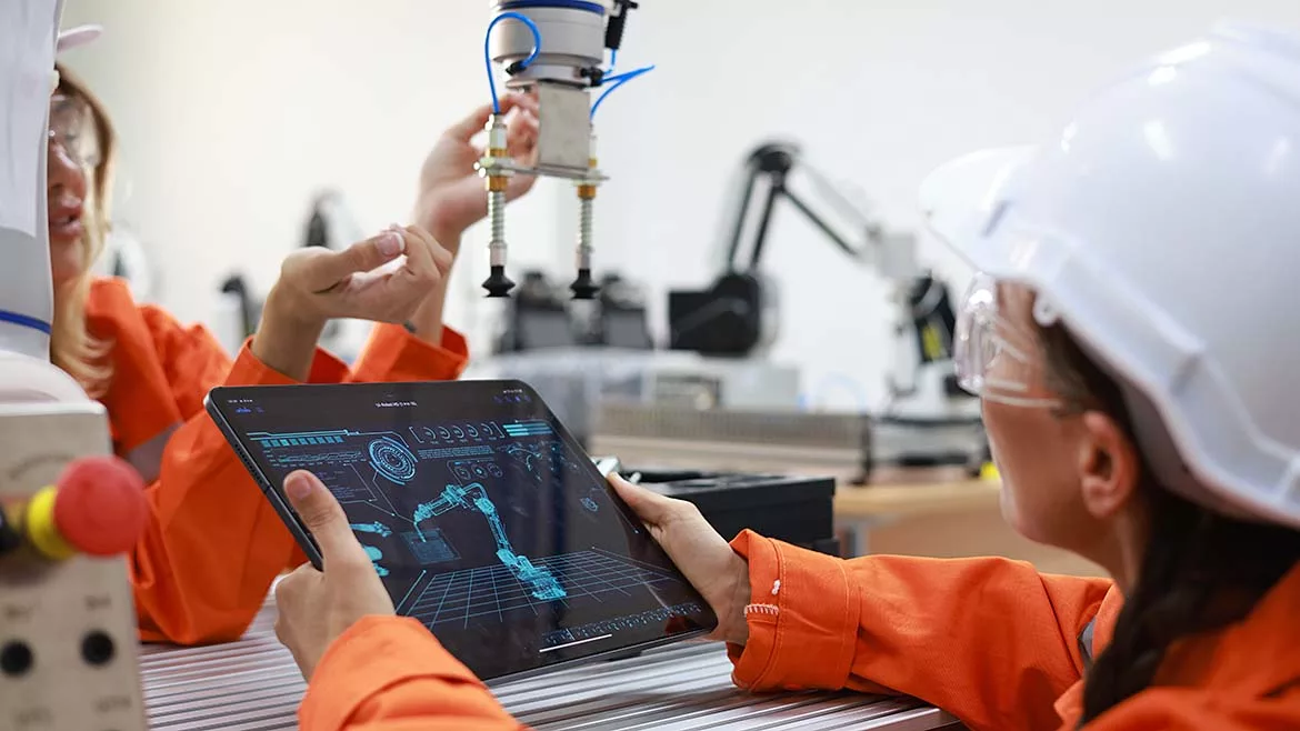 This image depicts a high-tech industrial robotics laboratory featuring workers interacting with robotic arms.