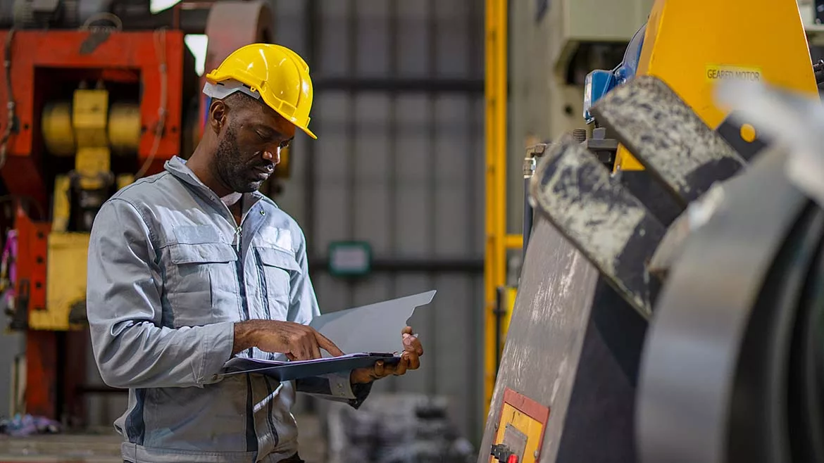 This image depicts a professional engineer or industrial worker inspecting machinery inside a factory.