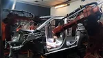 This image displays a modern automotive assembly line featuring industrial robots performing welding operations on a car body. 