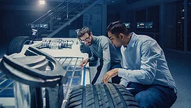 The image depicts engineers working on the development and safety testing of an electric vehicle chassis
